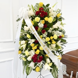 Standing floral spray with red, yellow, and white flowers and a white ribbon