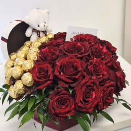 Red roses with gold-wrapped chocolates and a small teddy bear in a box
