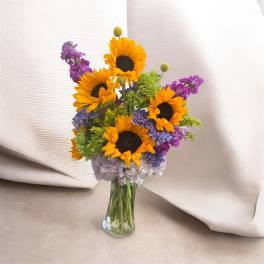 Bouquet of sunflowers and purple flowers in a clear glass vase