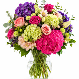 Mixed bouquet of pink, purple, and cream flowers in a clear glass vase
