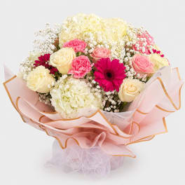 Bouquet of pink and cream roses, carnations, and hydrangeas wrapped in pale pink paper
