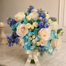 Wedding bouquet of cream roses, blue hydrangeas, and purple flowers tied with a satin ribbon