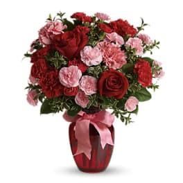 Red roses and pink carnations in a red vase with a pink ribbon