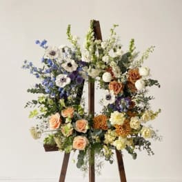 Large floral arrangement on a wooden easel with roses, anemones, and mixed blooms