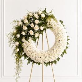 White floral wreath on a gold stand with roses and chrysanthemums