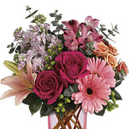 Mixed bouquet of pink roses, lilies, and gerbera daisies in a pink glass vase