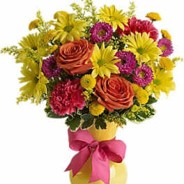 Colorful bouquet of roses, daisies, and carnations in a yellow vase with a pink ribbon.