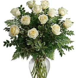 White roses arranged in a clear glass vase with dense greenery