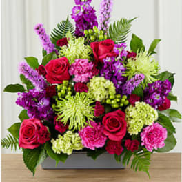 Mixed bouquet of red roses, purple flowers, and green blooms in a rectangular vase