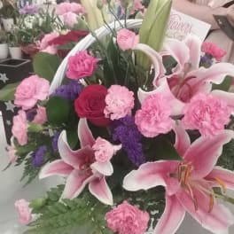 Pink lilies and carnations arranged with roses in a white basket