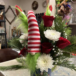Christmas arrangement with red roses, white mums, and a striped gnome in a holiday tin