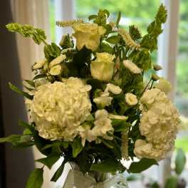 White floral arrangement in a clear glass vase with a ribbon bow