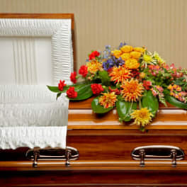Bright autumn-toned casket spray of mixed flowers on a wooden casket