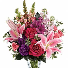 Mixed bouquet of pink lilies, roses, and purple flowers in a clear glass vase