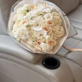 Bouquet of white orchids, cream roses, and hydrangeas wrapped in clear paper