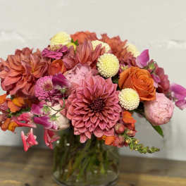 Mixed bouquet of pink, orange, and cream flowers in a glass vase
