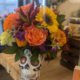 Bright flower arrangement with sunflower, roses, and marigolds in a painted sugar skull vase