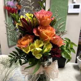 Bouquet of orange roses and yellow flowers in a glass vase with a ribbon