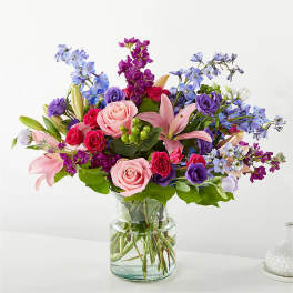 Mixed bouquet of pink roses, lilies, and blue flowers in a glass vase