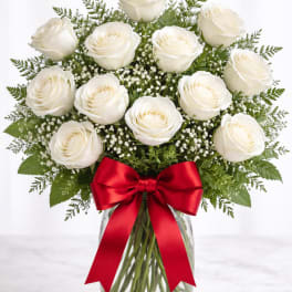 White roses arranged in a glass vase with a red ribbon
