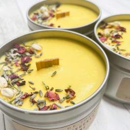 Three yellow candles in round tins topped with dried flower petals