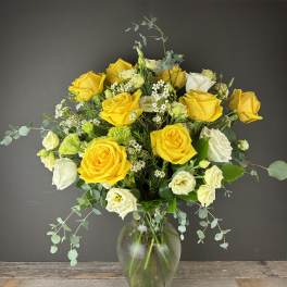 Yellow and white roses in a clear glass vase with airy filler flowers