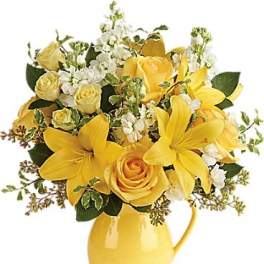 Yellow roses and lilies arranged in a yellow pitcher vase