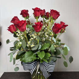 Red roses arranged in a clear glass vase with a striped ribbon.