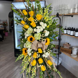 Tall floral standing spray with yellow and white roses, sunflowers, and a burlap bow