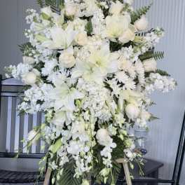 Large white floral standing spray with lilies, roses, and orchids on an easel