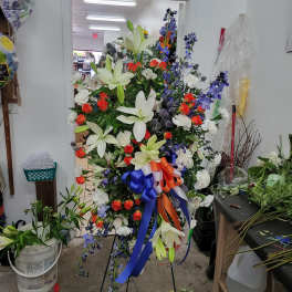 Large standing floral spray with white lilies, orange roses, and blue ribbon