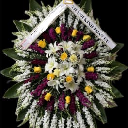 Large standing floral wreath with white lilies, yellow roses, and purple flowers