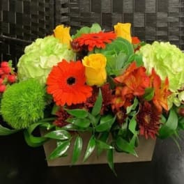 Bright mixed flower arrangement in a rectangular box with orange and yellow blooms