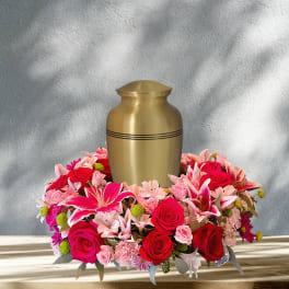 Pink and red floral arrangement around a gold urn