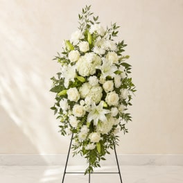 White funeral spray on a standing easel with lilies, roses, and hydrangeas