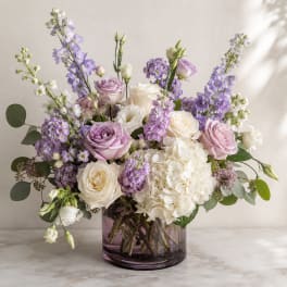 Lavender and white floral arrangement in a purple glass vase