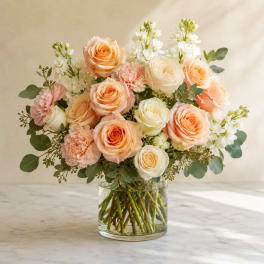 Peach and white roses with pink carnations in a clear glass vase