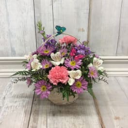 Basket arrangement of pink and purple flowers with a butterfly pick