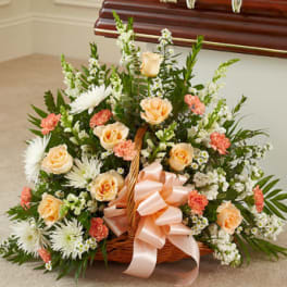 Basket arrangement of peach roses, white daisies, and pink carnations with a ribbon bow