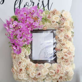 Floral frame of pink orchids and cream roses around a photo opening