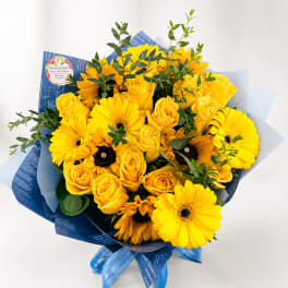 Yellow roses and gerbera daisies in blue wrapping with ribbon