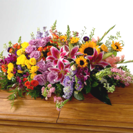 Colorful floral spray with lilies, roses, and sunflowers on a wooden casket