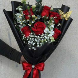 Bouquet of red roses with white filler flowers wrapped in black paper and a red ribbon
