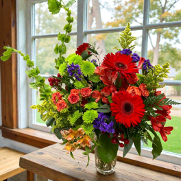 Bright mixed bouquet in a clear glass vase with red gerbera daisies and orange roses