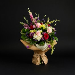 Mixed bouquet of roses, hydrangeas, and purple blooms wrapped in brown paper