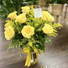 Yellow roses arranged in a glass vase with yellow ribbon
