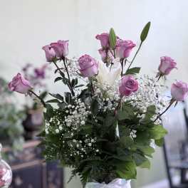 Pink roses and white lilies in a clear glass vase with a white ribbon