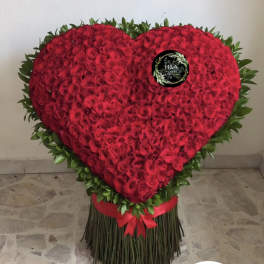 Heart-shaped arrangement of red roses with a green border and red ribbon