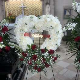Heart-shaped white floral wreath with red roses and a ribbon on an easel
