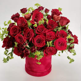 Arrangement of red roses with green accents in a red hatbox with glitter heart picks